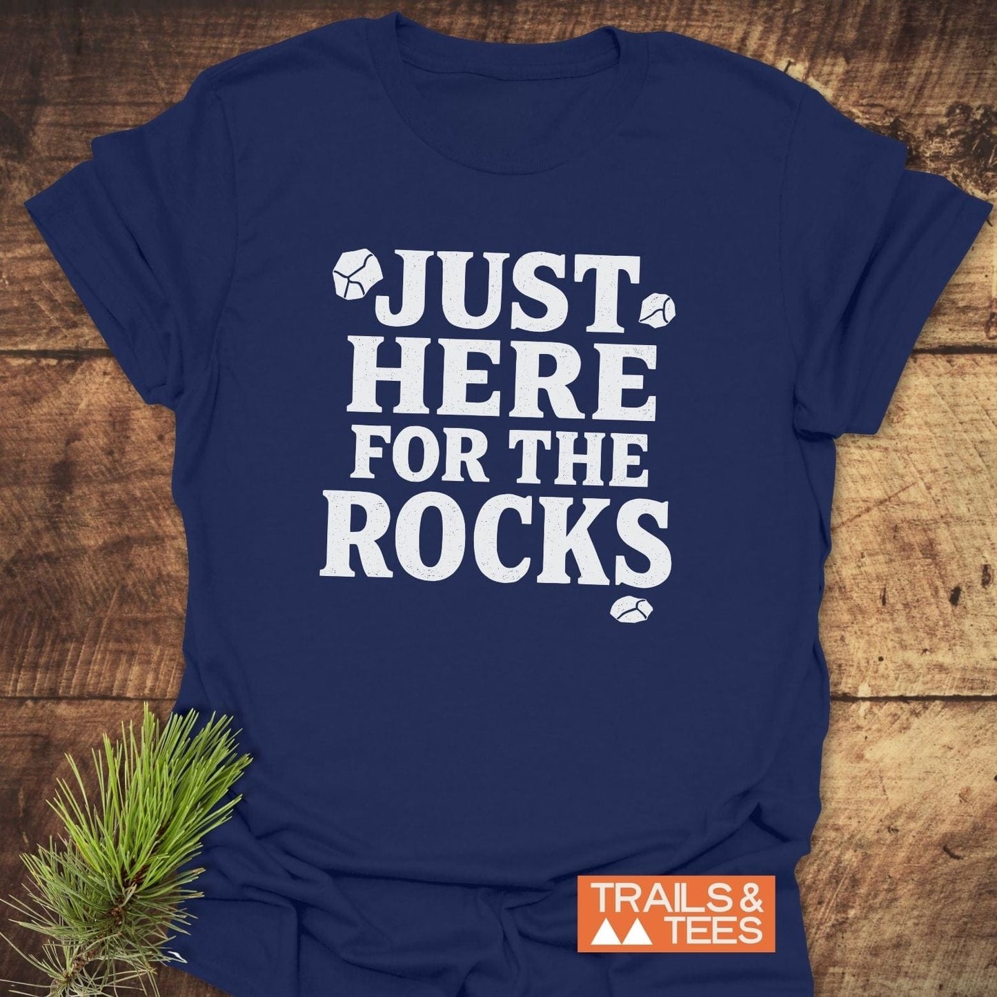 Navy T-shirt reading JUST HERE FOR THE ROCKS with rock illustrations, featuring the TRAILS & TEES logo, emphasizes outdoor adventures and comfort.