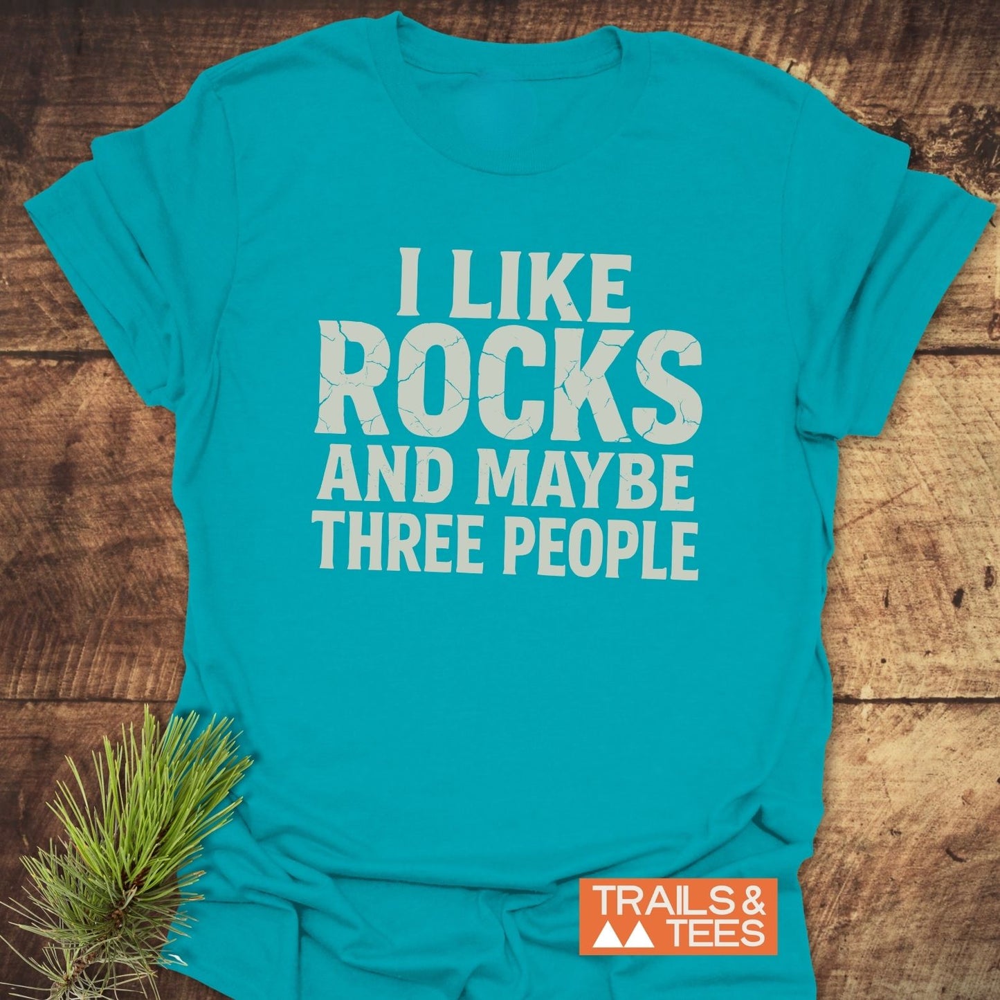 I Like Rocks T-Shirt featuring a humorous slogan, crafted from soft cotton with a Trails & Tees logo, designed for comfort and durability.