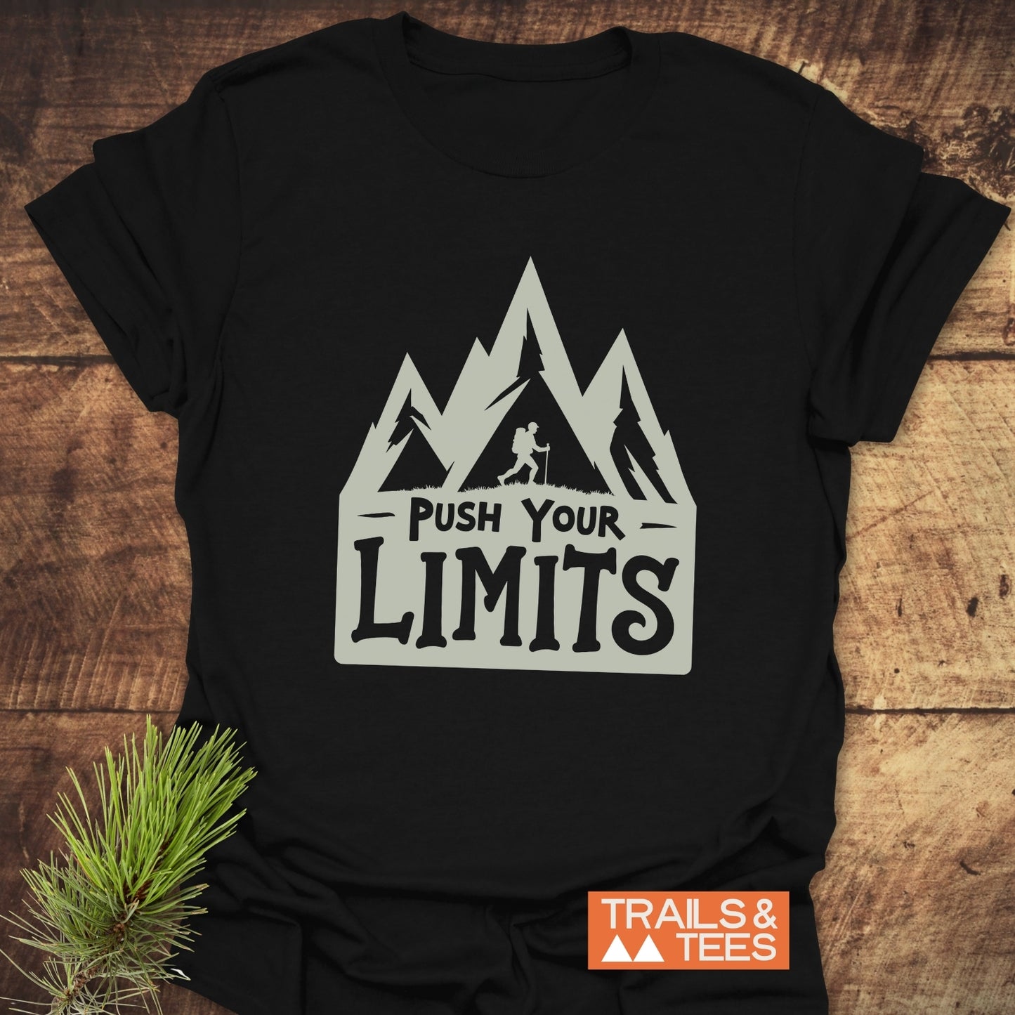 Push Your Limits T-Shirt featuring mountain peaks and hiker graphic; soft, durable cotton for outdoor adventures. Includes “TRAILS & TEES” logo.