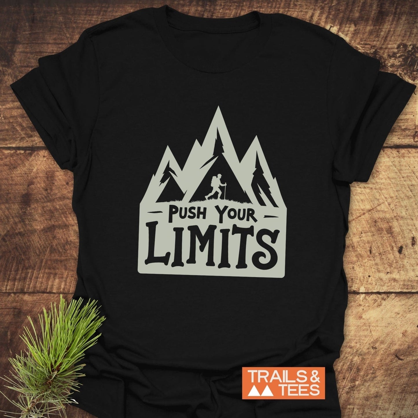 Push Your Limits T-Shirt featuring mountain peaks and hiker graphic; soft, durable cotton for outdoor adventures. Includes “TRAILS & TEES” logo.