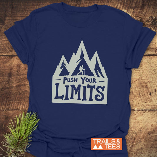 Push Your Limits T-Shirt featuring stylized mountain peaks and hiker graphic, laid flat on wood. Made from soft, lightweight cotton for everyday outdoor adventures.