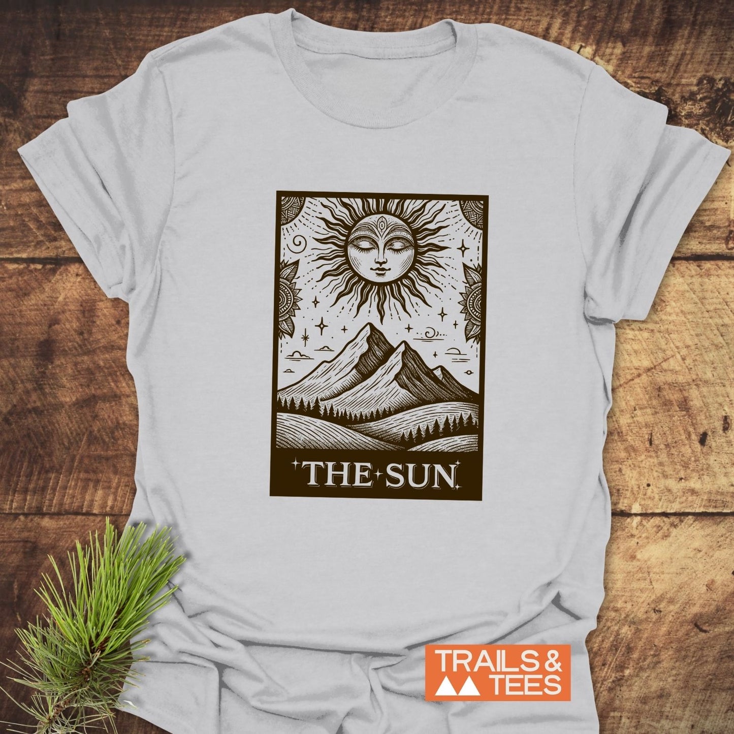 The Sun Tarot T-Shirt features a tarot-style sun graphic above mountains and trees, embodying Trails & Tees' comfort and outdoor spirit.
