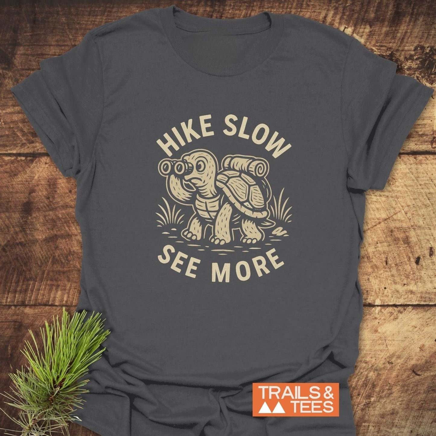 Hike Slow Funny T-Shirt: Dark-gray tee with a cream turtle print, promoting a mindful hiking message. Crafted from soft cotton, designed for durability and comfort.