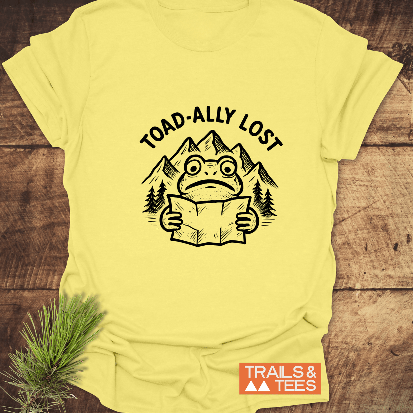 Toad-ally Lost T-Shirt features a toad with a map and mountain scene, printed on soft, durable cotton for outdoor enthusiasts.