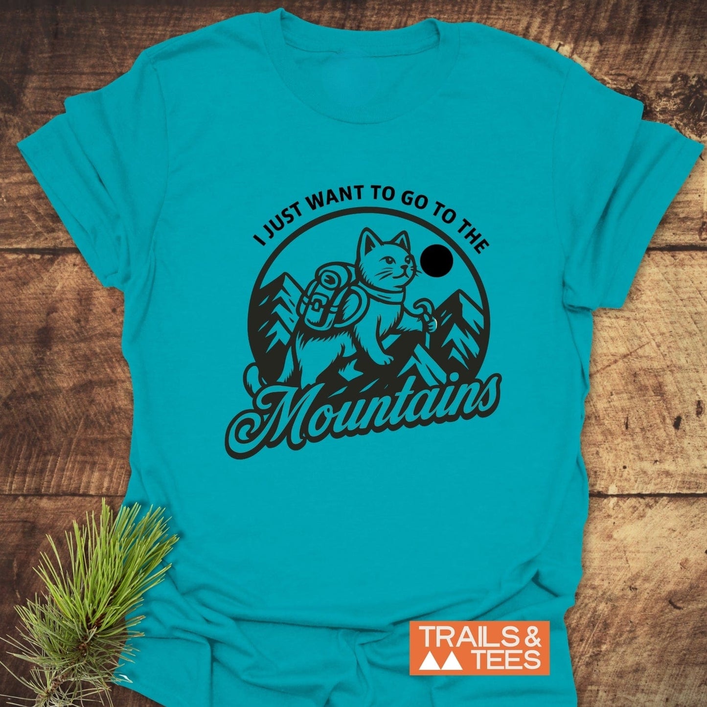 Mountain Kitty T-Shirt featuring a cat graphic with a backpack and hiking stick, surrounded by mountains and sun, emphasizing outdoor adventure spirit.