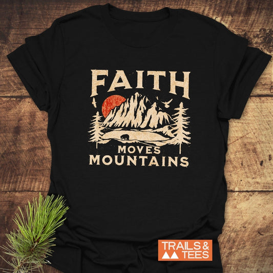 Faith Moves Mountains T-Shirt featuring a mountain scene with a red sun, pine trees, bear silhouette, and birds. Soft cotton, pre-shrunk, durable print.