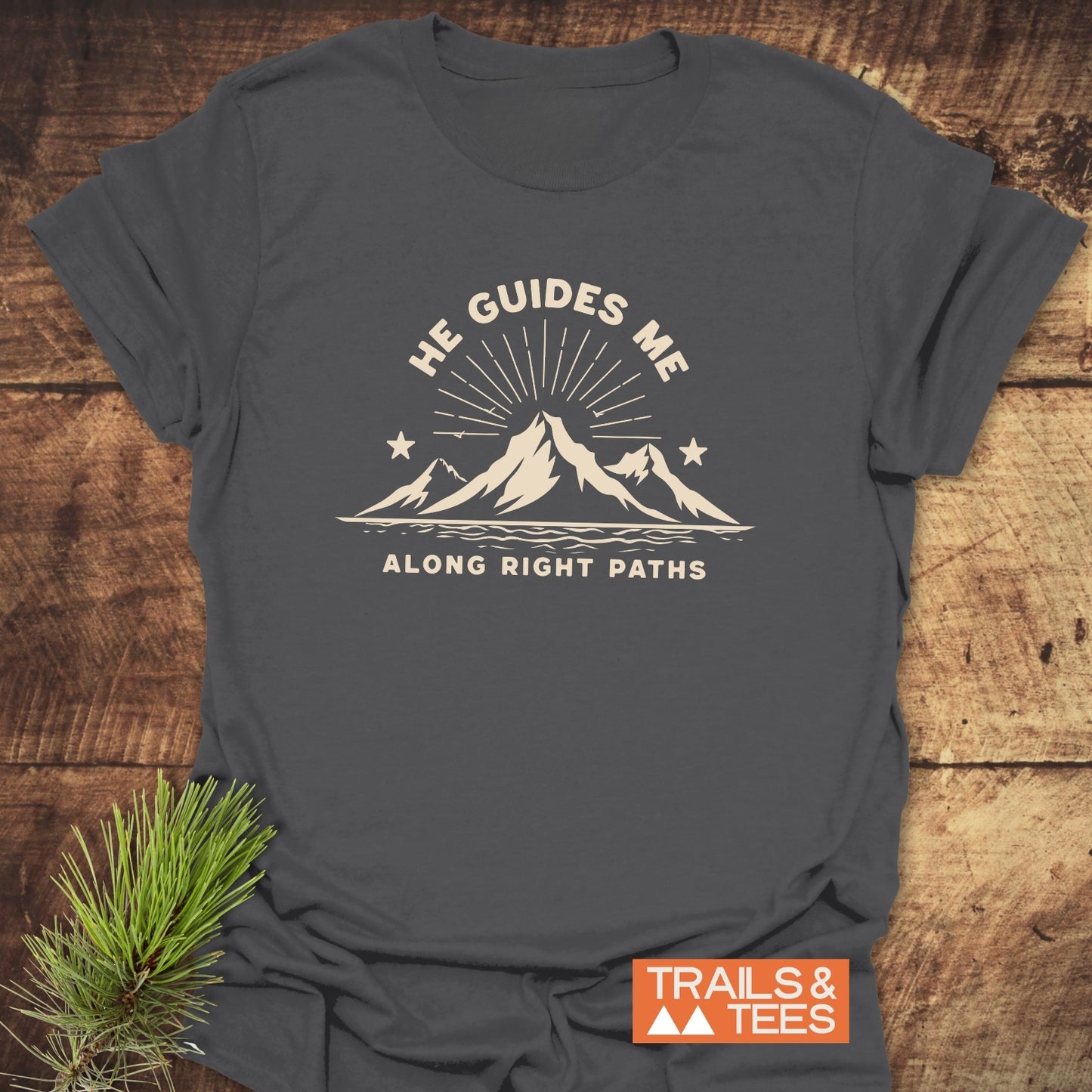 He Guides Me T-Shirt with mountain design and sunbeams, crafted from soft cotton for comfort and durability, featuring the Trails & Tees logo on the corner.