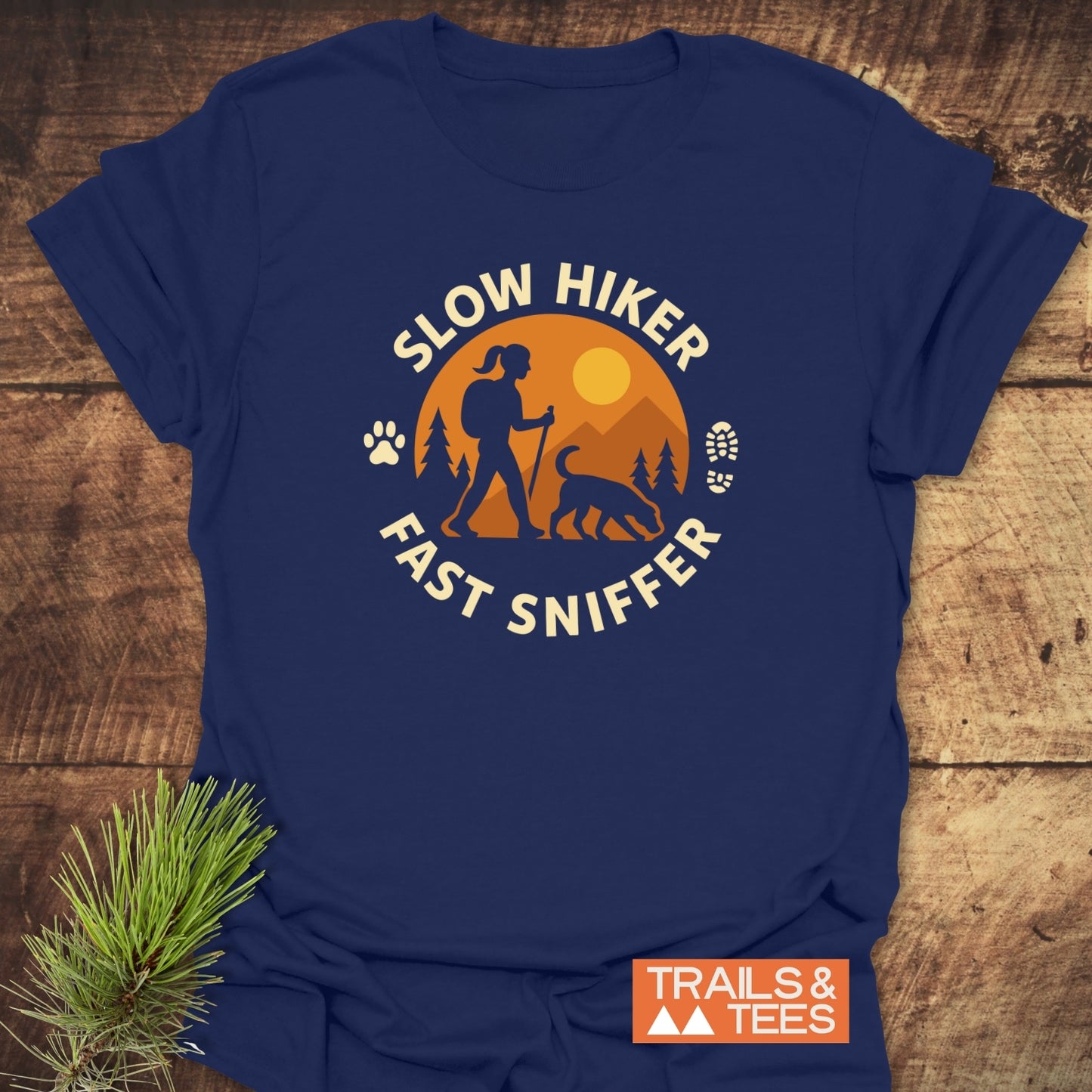 Navy-blue Fast Sniffer T-Shirt with a hiker and dog graphic, SLOW HIKER, FAST SNIFFER text, paw print, boot icon, sun, mountains, and TRAILS & TEES logo.