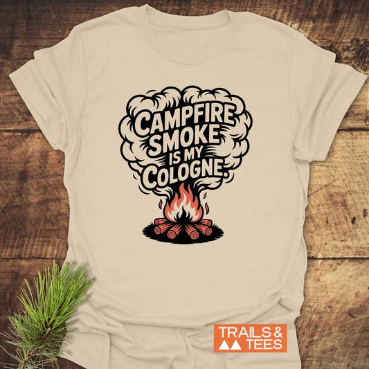 Campfire Smoke Funny T-Shirt featuring a campfire graphic and playful text, styled with a pine sprig, showcases comfort and adventure-ready design.