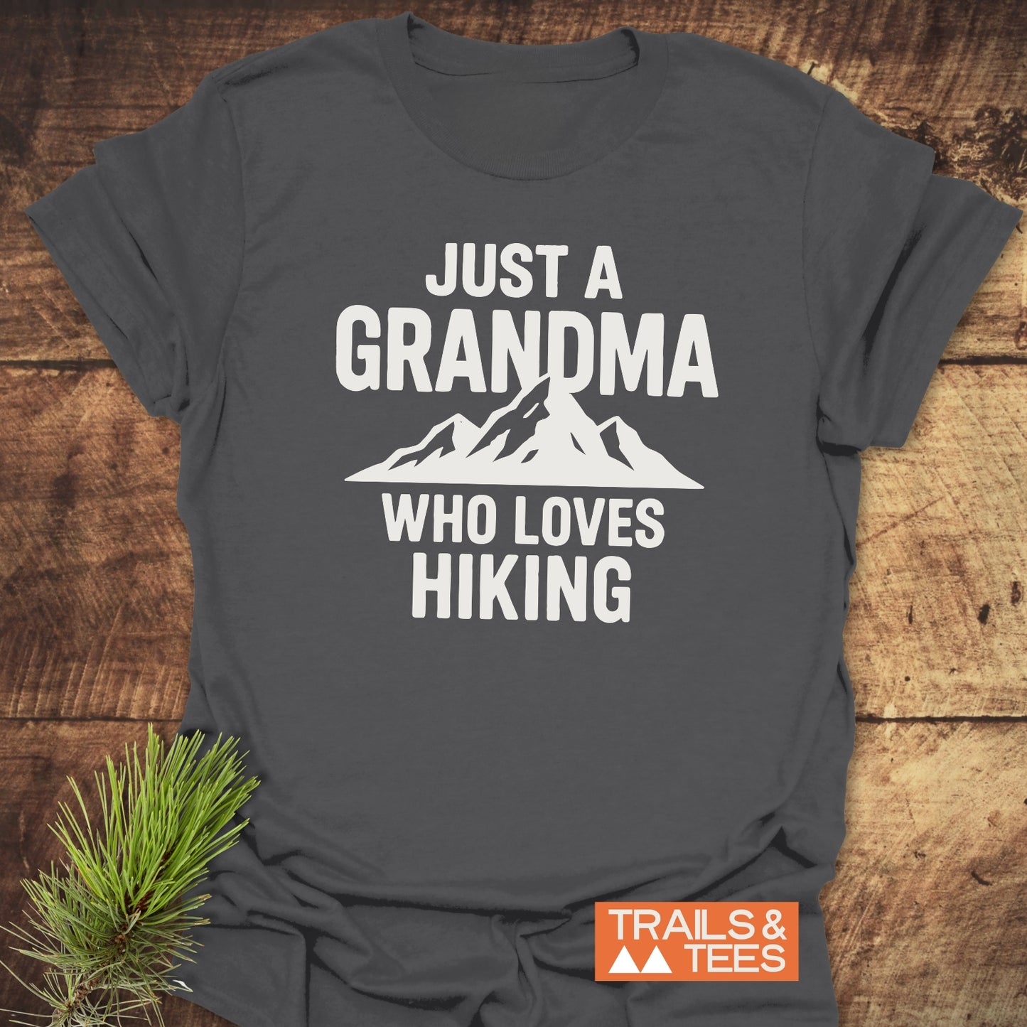 Grandma Loves Hiking T-Shirt with mountain graphic, laid on wood, embodying comfort and durability. Features soft cotton, pre-shrunk fit, and eco-friendly print.