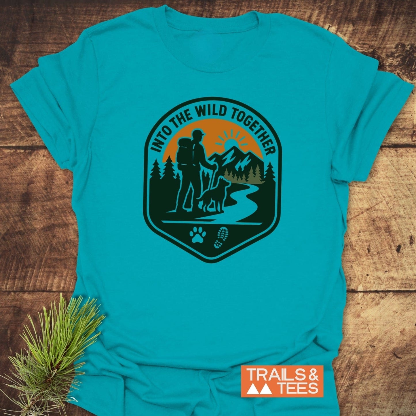 Into The Wild T-Shirt featuring a backpacker and dog print with pine trees and mountains. Lightweight cotton, durable print, ideal for outdoor enthusiasts.
