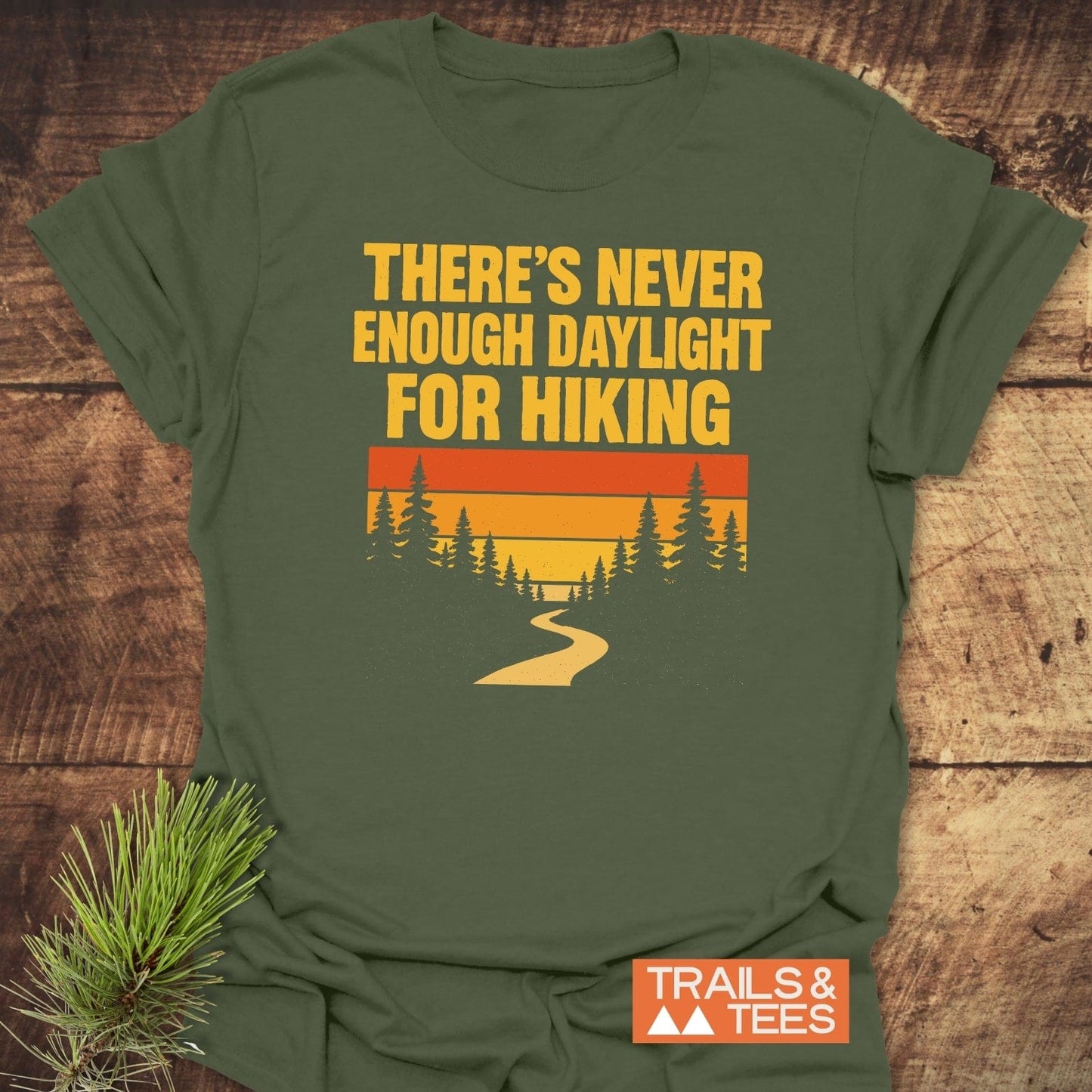 Never Enough T-Shirt featuring retro forest graphic and hiking quote, made of soft ring-spun cotton with durable print. Laid flat with pine sprig.