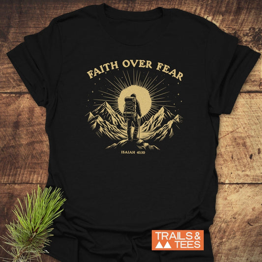 Faith Over Fear T-Shirt on rustic wood, features gold graphic of backpacker on mountain with ISAIAH 41:10 citation; durable, lightweight cotton for outdoor enthusiasts.
