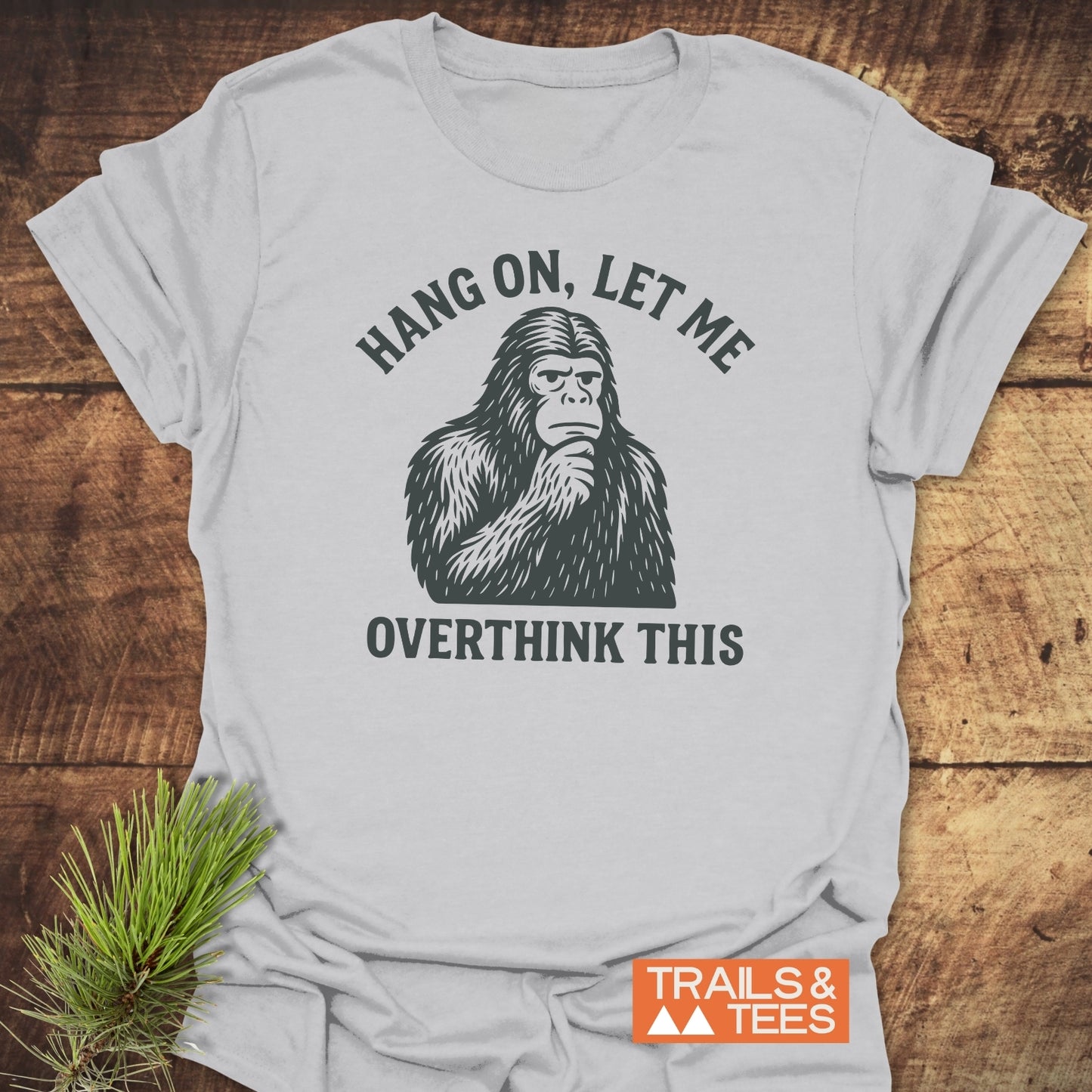 Bigfoot Overthinking T-Shirt featuring a thoughtful ape-like creature and the text “HANG ON, LET ME OVERTHINK THIS,” designed for comfort and outdoor adventures.