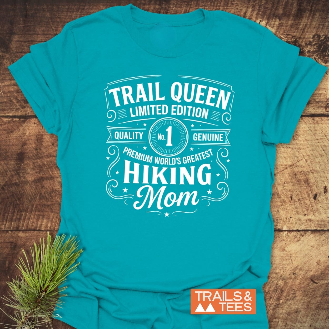 Trail Queen Mom T-Shirt on wooden surface with pine sprig, featuring a white graphic. Durable, soft ring-spun cotton, pre-shrunk, and eco-friendly.