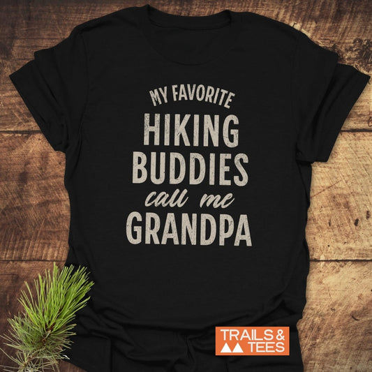 Black Hiking Grandpa T-Shirt with off-white slogan, crafted from soft cotton, featuring durable prints and taped shoulders for comfort. Displayed on wooden surface with pine sprig.