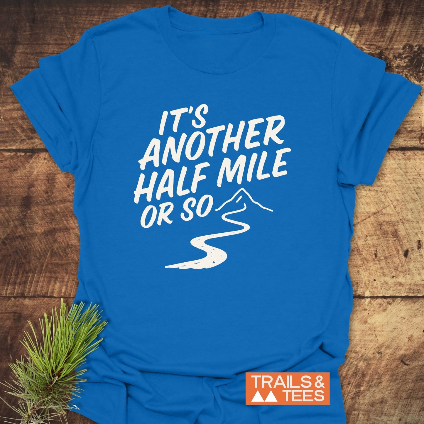 Half Mile Funny T-Shirt: Bright blue tee with mountain trail graphic, slogan, and Trails & Tees logo, crafted from soft cotton for outdoor enthusiasts.