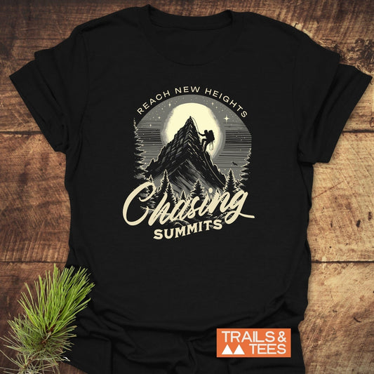 Black Chasing Summits T-shirt with vintage graphic of climber on mountain, full moon, and pine trees. Includes REACH NEW HEIGHTS text. Styled with evergreen.