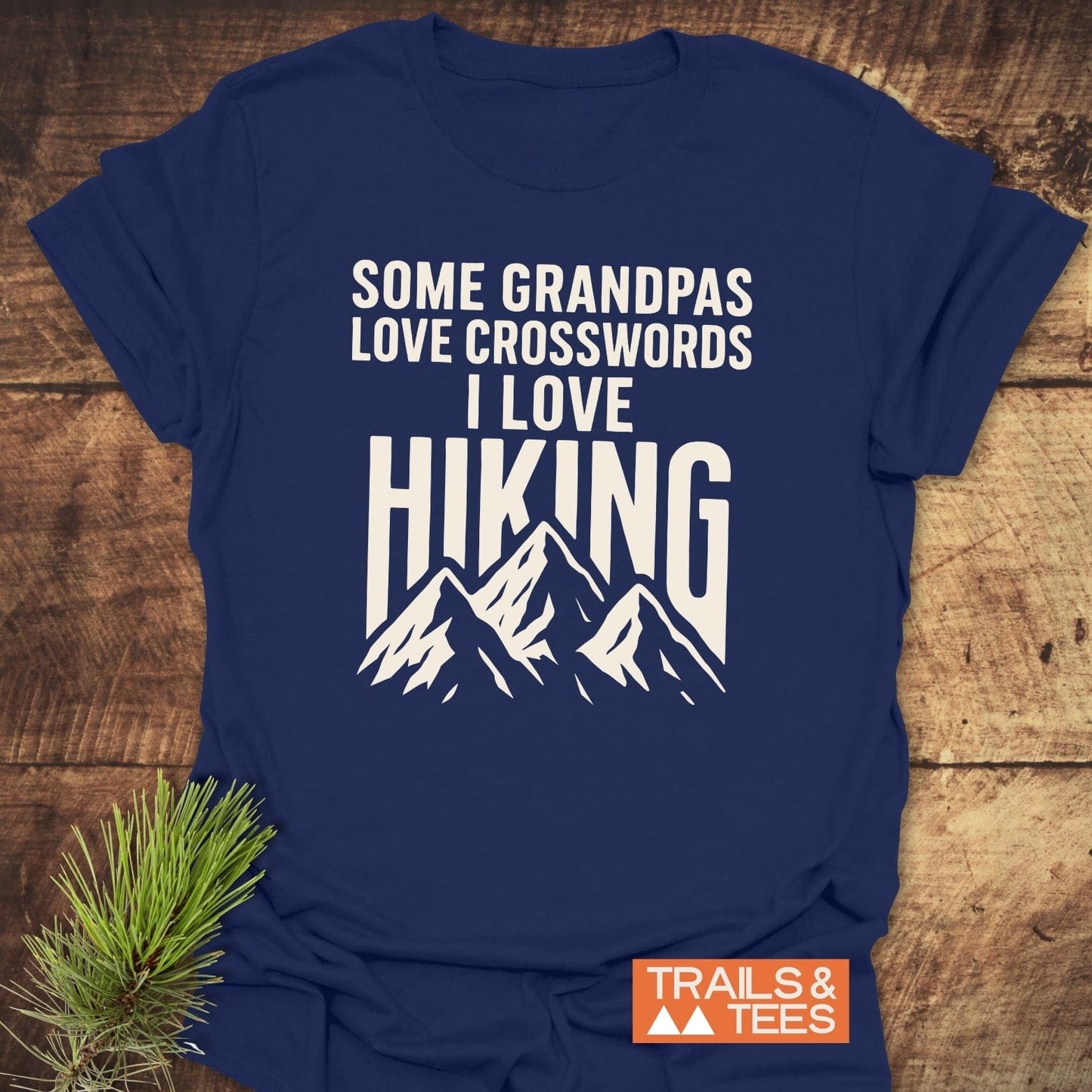 Navy-blue Grandpa Loves Hiking T-shirt with white mountain peaks design, laid on wood. Soft, lightweight cotton for adventure lovers, featuring durable prints.