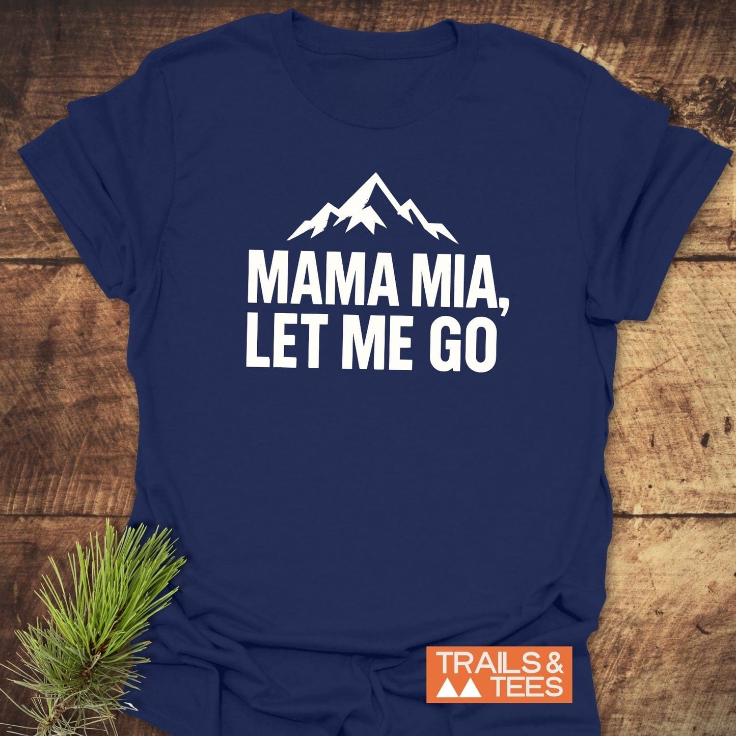 Let Me Go Funny T-Shirt featuring mountain peaks graphic, “MAMA MIA, LET ME GO” text, crafted from soft cotton, with durable prints and Trails & Tees logo.