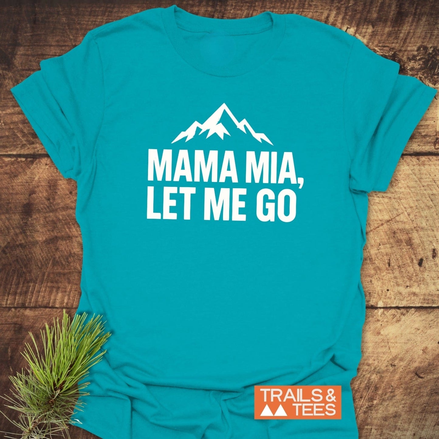 Let Me Go Funny T-Shirt: Teal shirt with mountain silhouette and bold text, showcasing comfort and durability, branded by Trails & Tees, with nature-inspired elements.