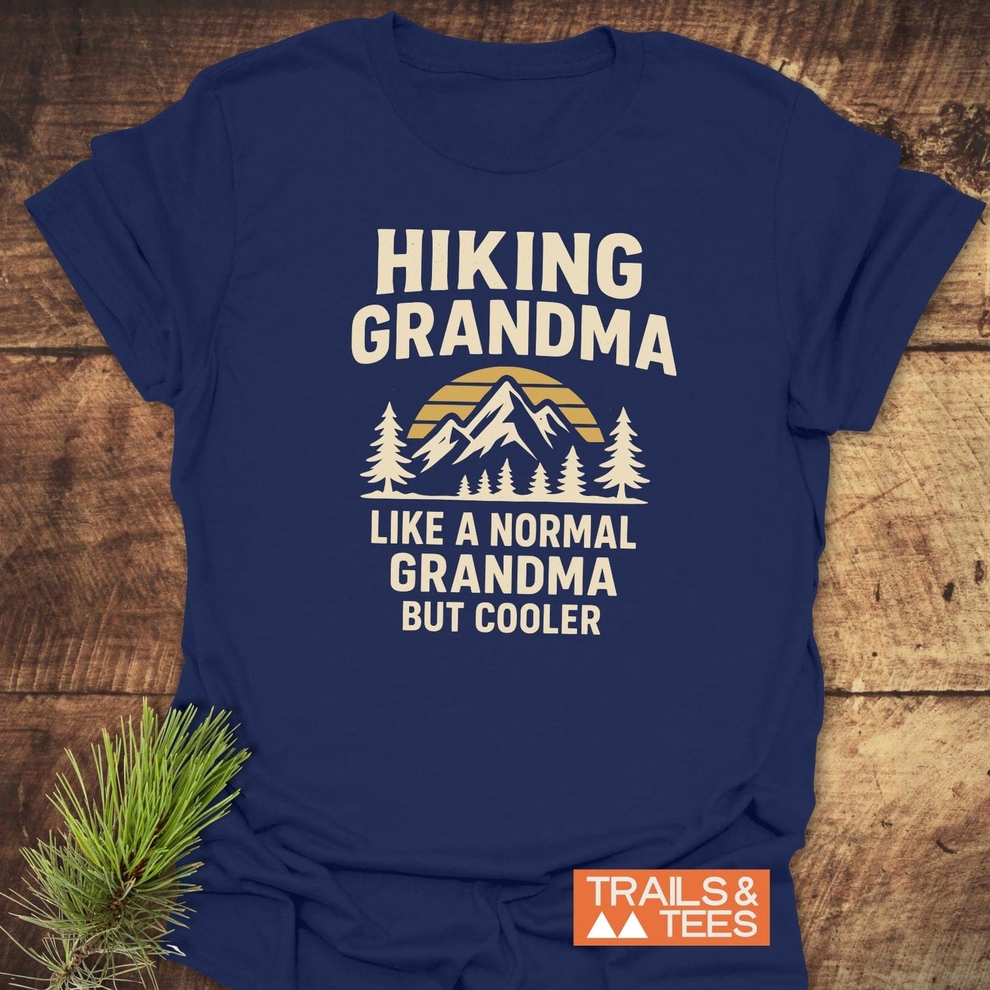Navy blue Hiking Grandma Sunrise T-Shirt with mountain graphic and slogans, designed for comfort and durability, laid flat with pine sprig accent.