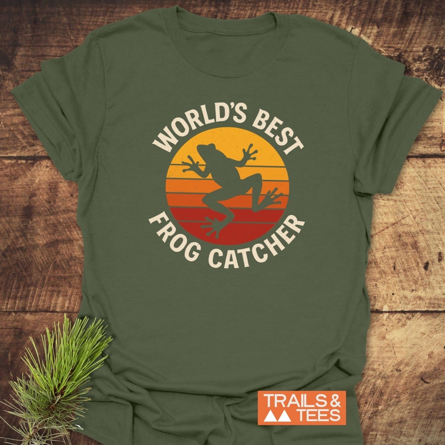 Frog Catcher T-Shirt featuring a retro-style leaping frog graphic on green cotton, highlighting outdoor adventure spirit. Includes Trails & Tees logo for brand authenticity.