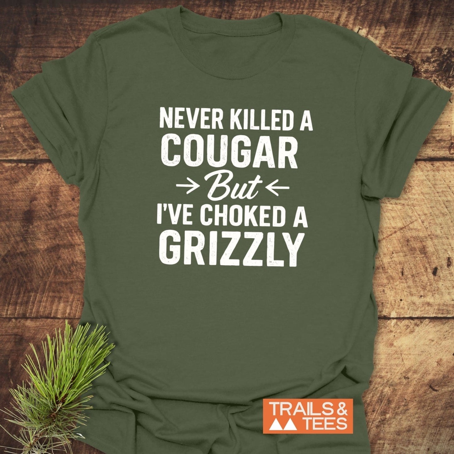 Never Killed A Cougar T-Shirt on rustic wood, showcasing bold slogan in white. Features soft cotton, durable print, and taped shoulders for comfort and lasting shape.