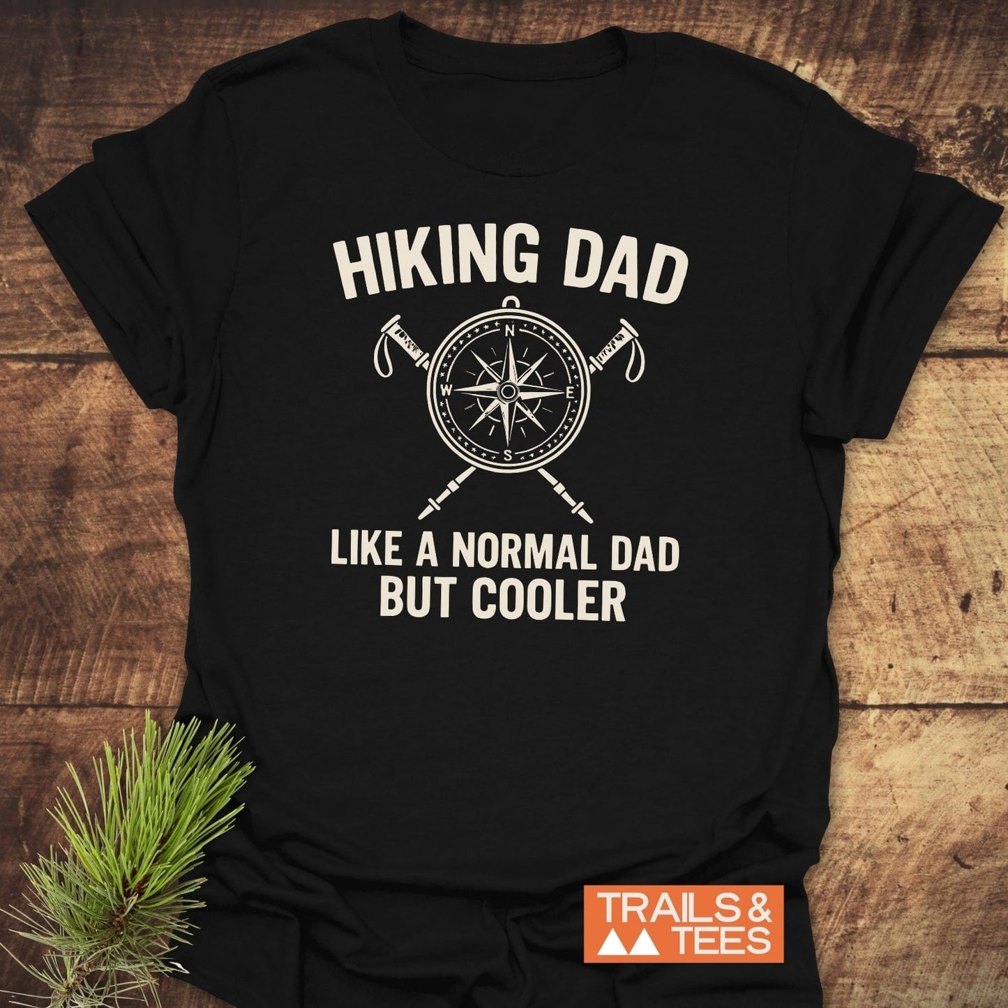 Black T-shirt with HIKING DAD compass graphic, ideal for outdoor enthusiasts. Made from soft cotton, featuring durable prints. Logo: TRAILS & TEES.