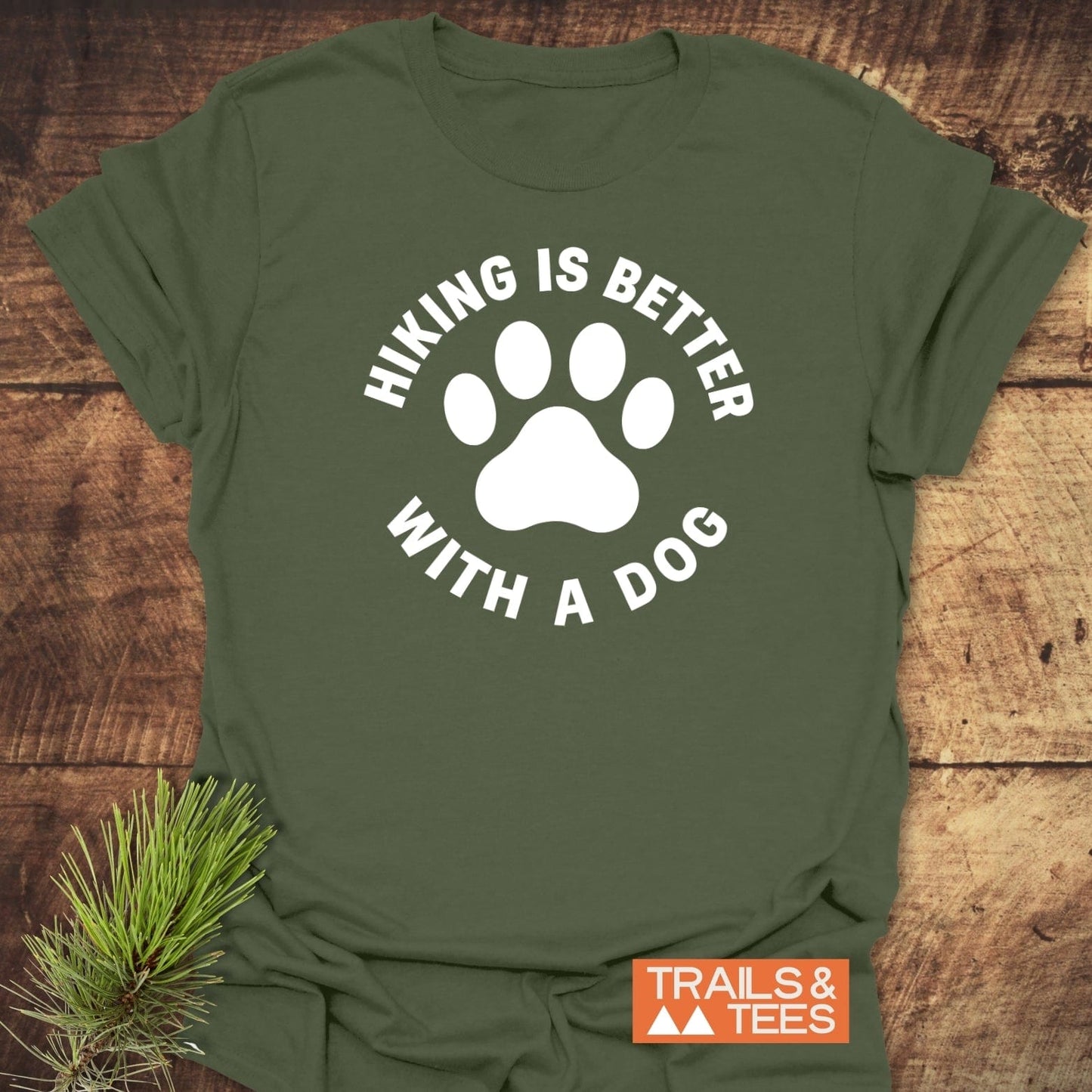 Hiking With Dogs T-Shirt featuring a dog-paw graphic and “HIKING IS BETTER WITH A DOG” text on soft, ring-spun cotton, styled with pine sprig.