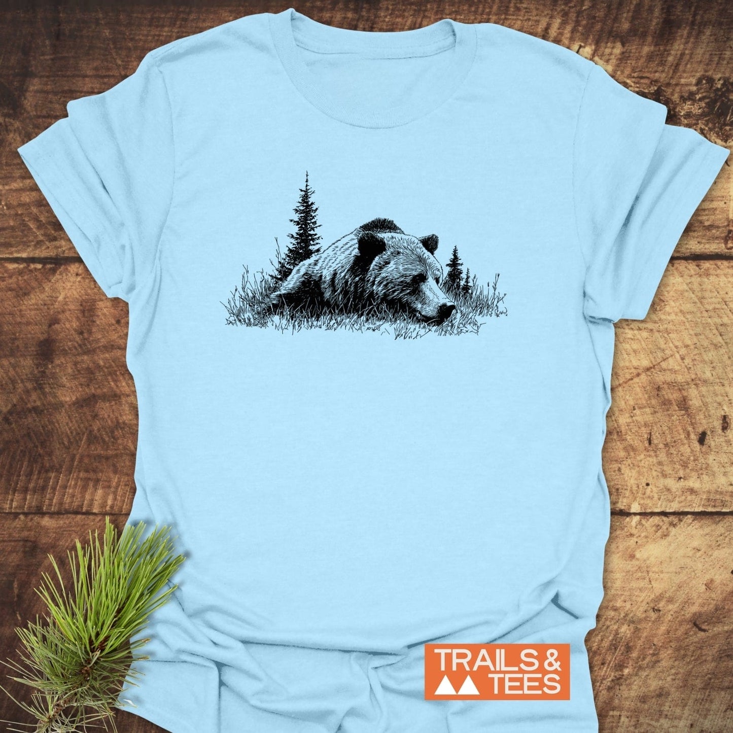 Relaxing Grizzly T-Shirt featuring a bear and pine trees design on soft ring-spun cotton, showcasing durability and outdoor-inspired comfort, with TRAILS & TEES logo.