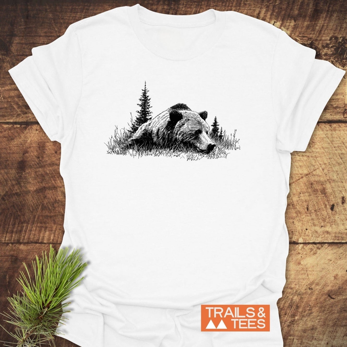 Relaxing Grizzly T-Shirt features a black bear design on soft, ring-spun cotton, highlighting outdoor adventure with a small TRAILS & TEES logo.