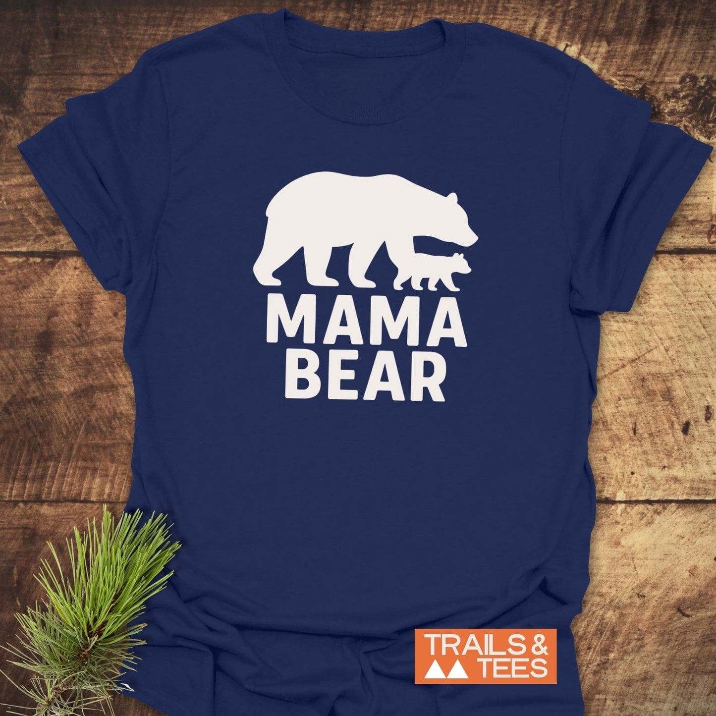 Mama Bear T-Shirt featuring a bear and cub silhouette, with “TRAILS & TEES” logo, laid on wood. Soft, durable cotton for outdoor adventures.