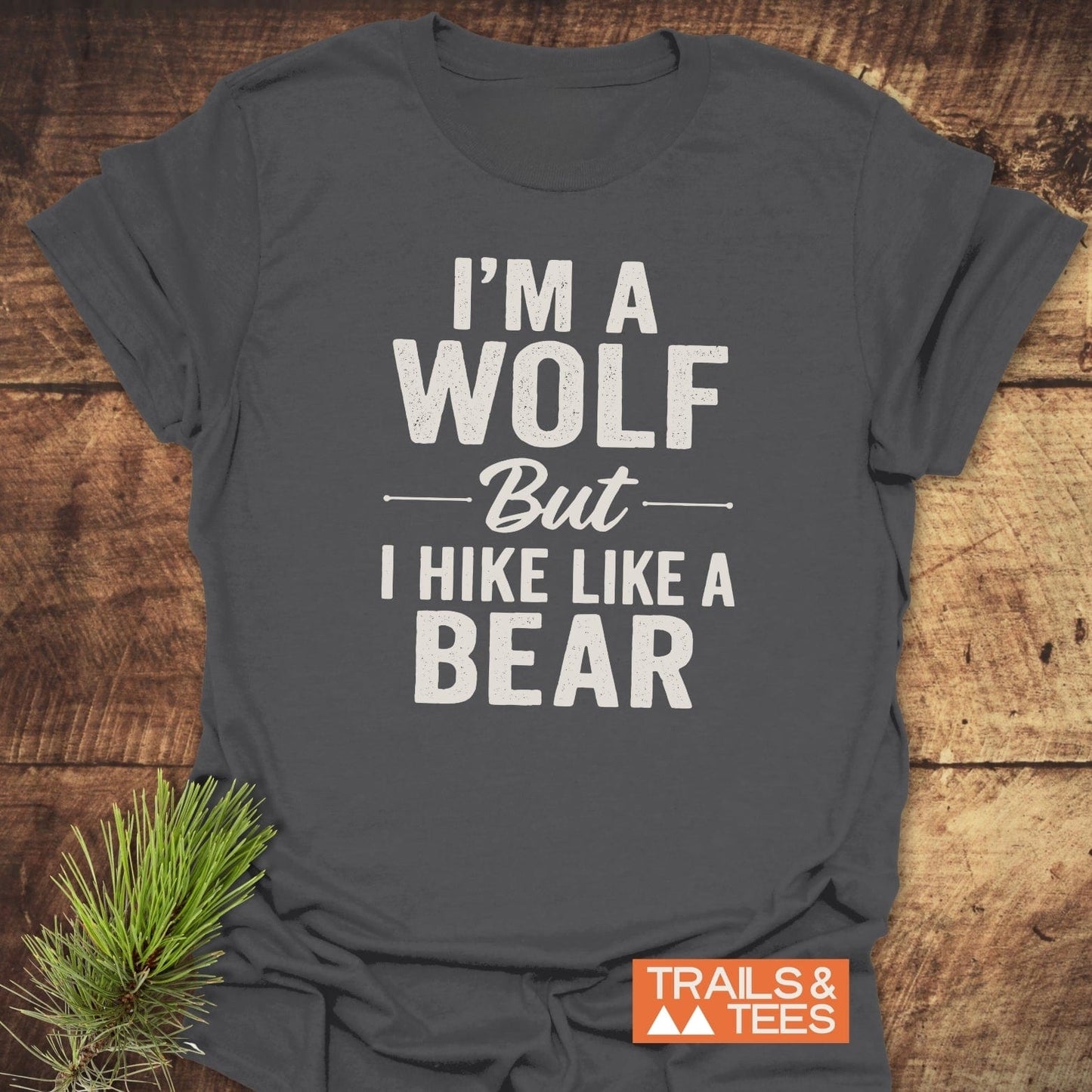 Dark-gray I’m A Wolf Funny T-Shirt on rustic wood, featuring bold white text. Orange TRAILS & TEES. logo in corner. Soft, durable, adventure-ready design.