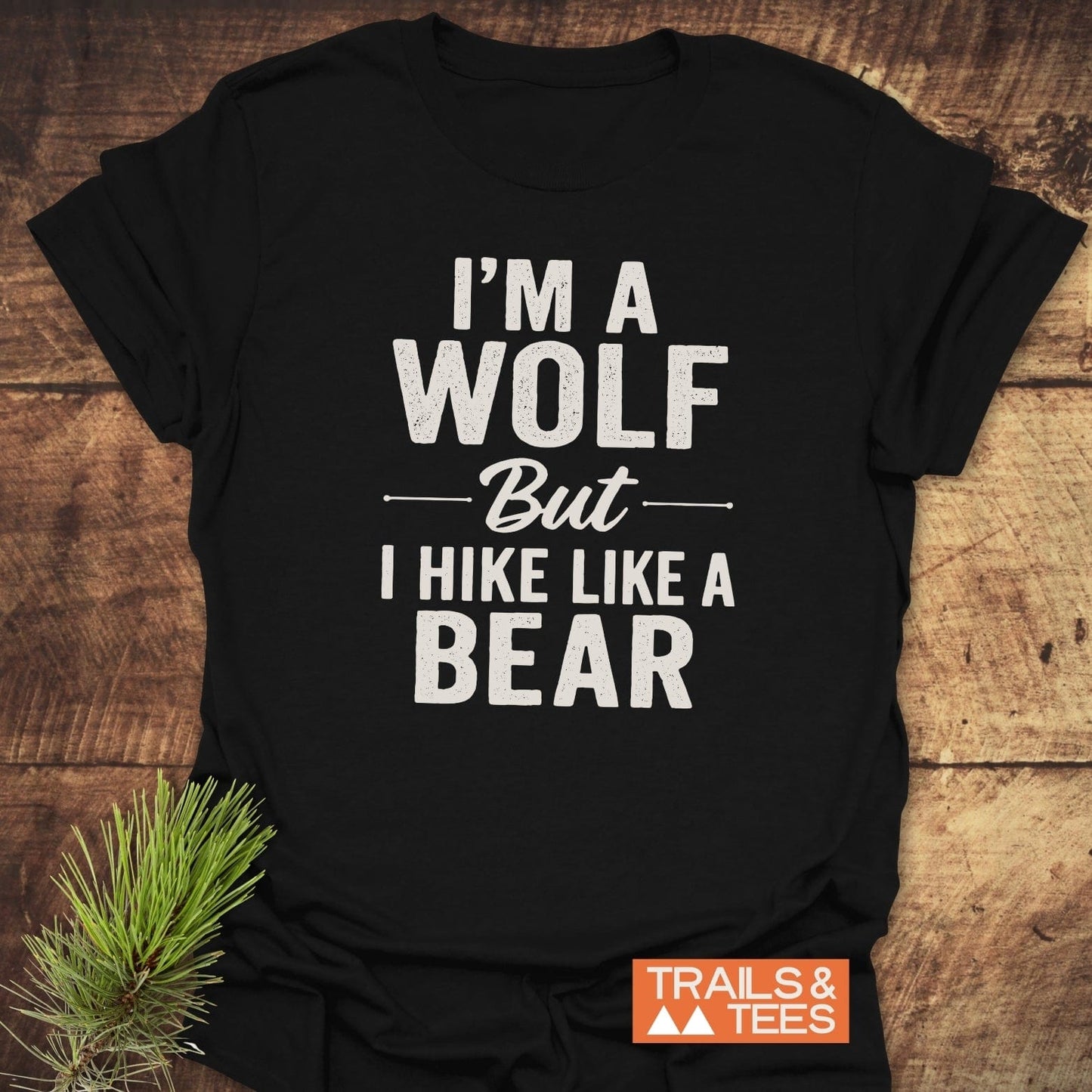 I'm A Wolf Funny T-Shirt with bold white slogan on a black tee, laid flat, featuring a small pine sprig and TRAILS & TEES tag.