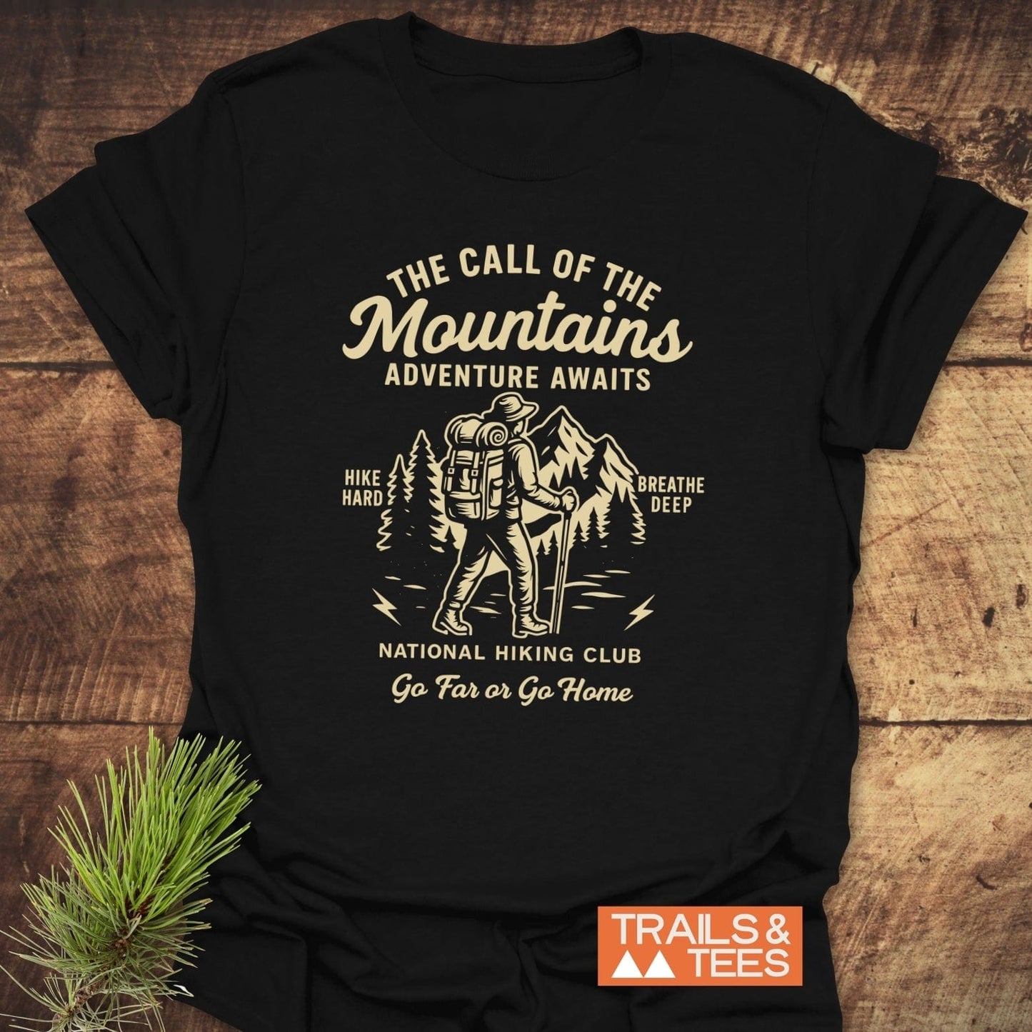 Call Of The Mountains T-Shirt: Black tee with cream hiker graphic and mountain scene, promoting adventure. Features durable print, soft cotton, no side seams.