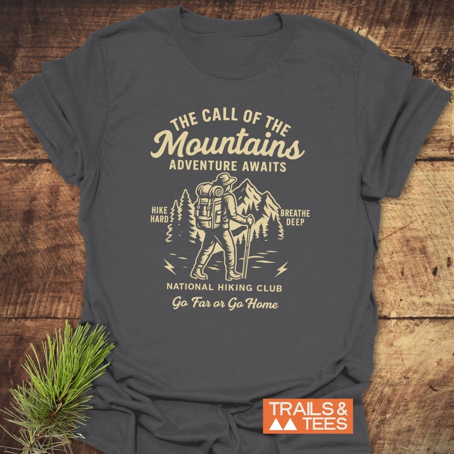 Call Of The Mountains T-Shirt with vintage hiker graphic and text, styled with a pine branch; made of soft cotton for outdoor enthusiasts.