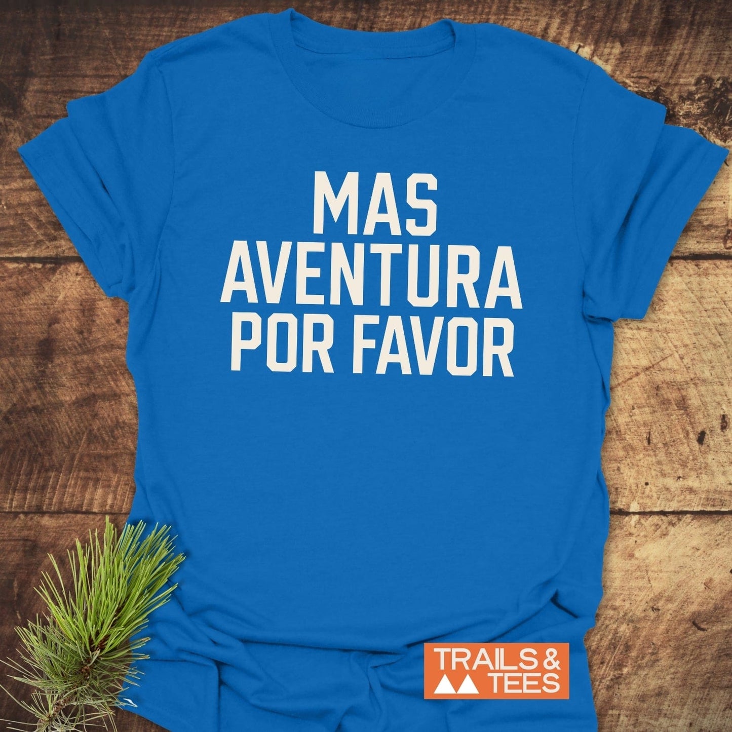 Mas Aventura T-Shirt laid flat, features bold white lettering and Trails & Tees logo, complemented by a pine sprig for an outdoorsy touch.