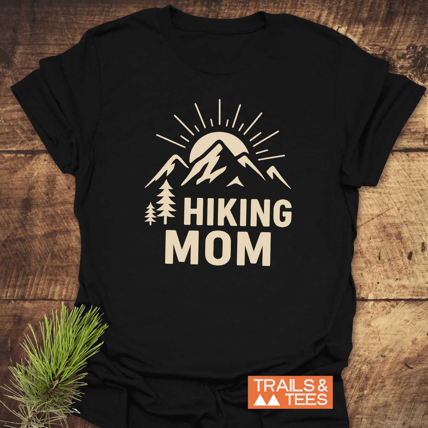 Hiking Mom Sunrise T-Shirt featuring a tan mountain graphic and “HIKING MOM” text, designed for comfort and outdoor enthusiasts, with a Trails & Tees logo.