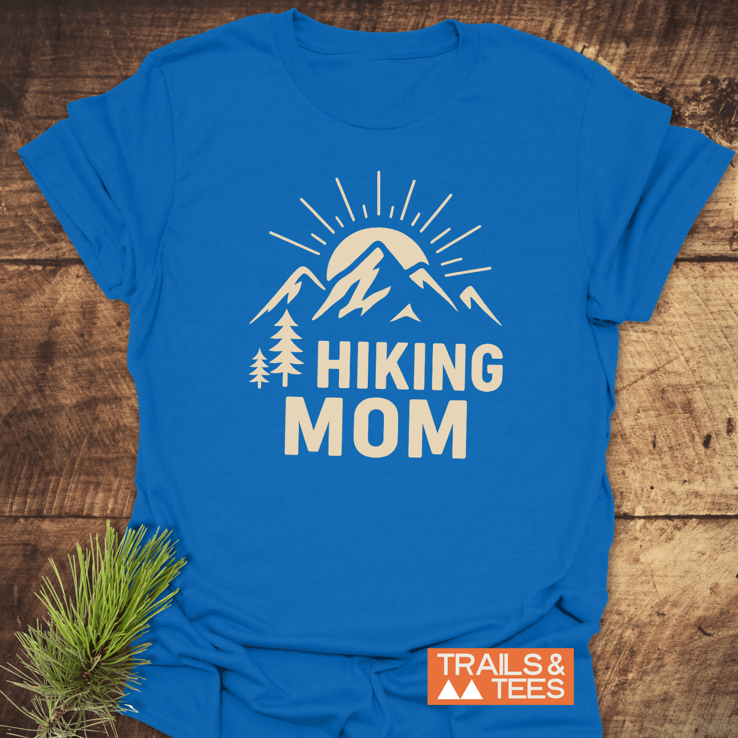 Hiking Mom Sunrise T-Shirt featuring a mountain and sun graphic with pine trees, laid flat, highlighting outdoor spirit and durable, soft cotton design.
