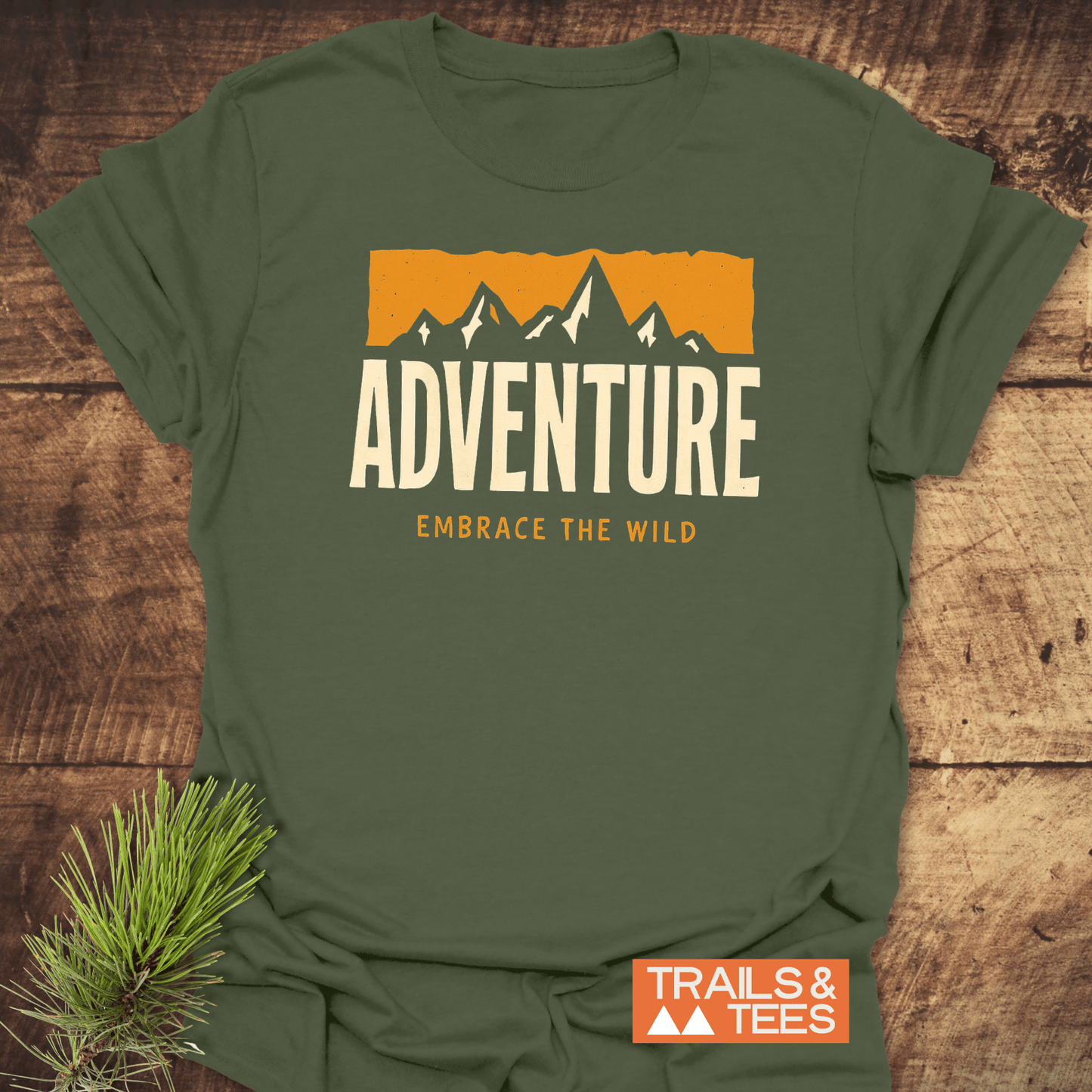 Adventure T-Shirt featuring gold mountain graphic and Embrace the Wild tagline, crafted from soft cotton for comfort and durability, alongside Trails & Tees logo.
