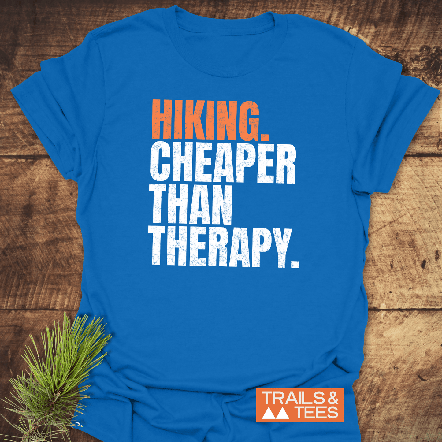 Hiking. Cheaper Than Therapy T-Shirt on rustic wood, featuring orange and white slogan. Includes Trails & Tees logo. Soft, lightweight ring-spun cotton.
