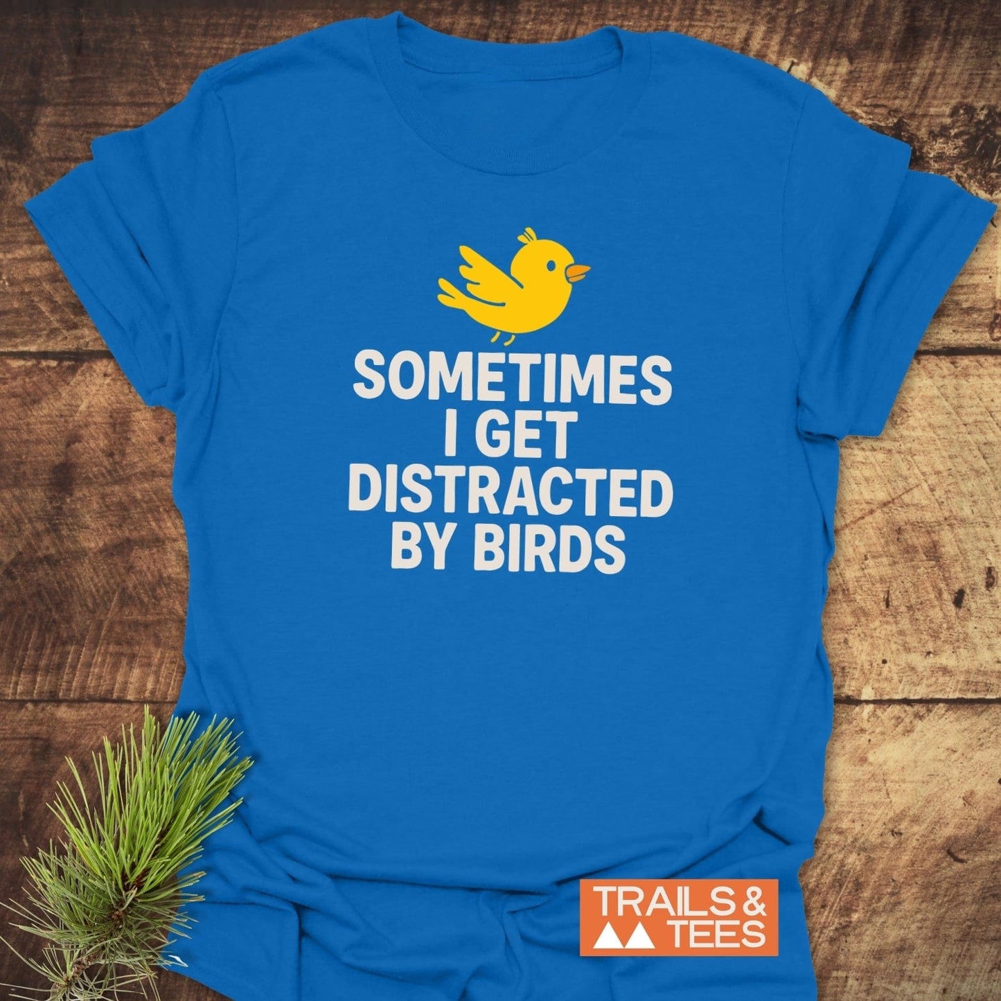Bird Distraction Funny T-Shirt featuring a yellow bird graphic and bold text, laid on wood. Soft cotton, pre-shrunk, durable print, perfect for outdoor enthusiasts.