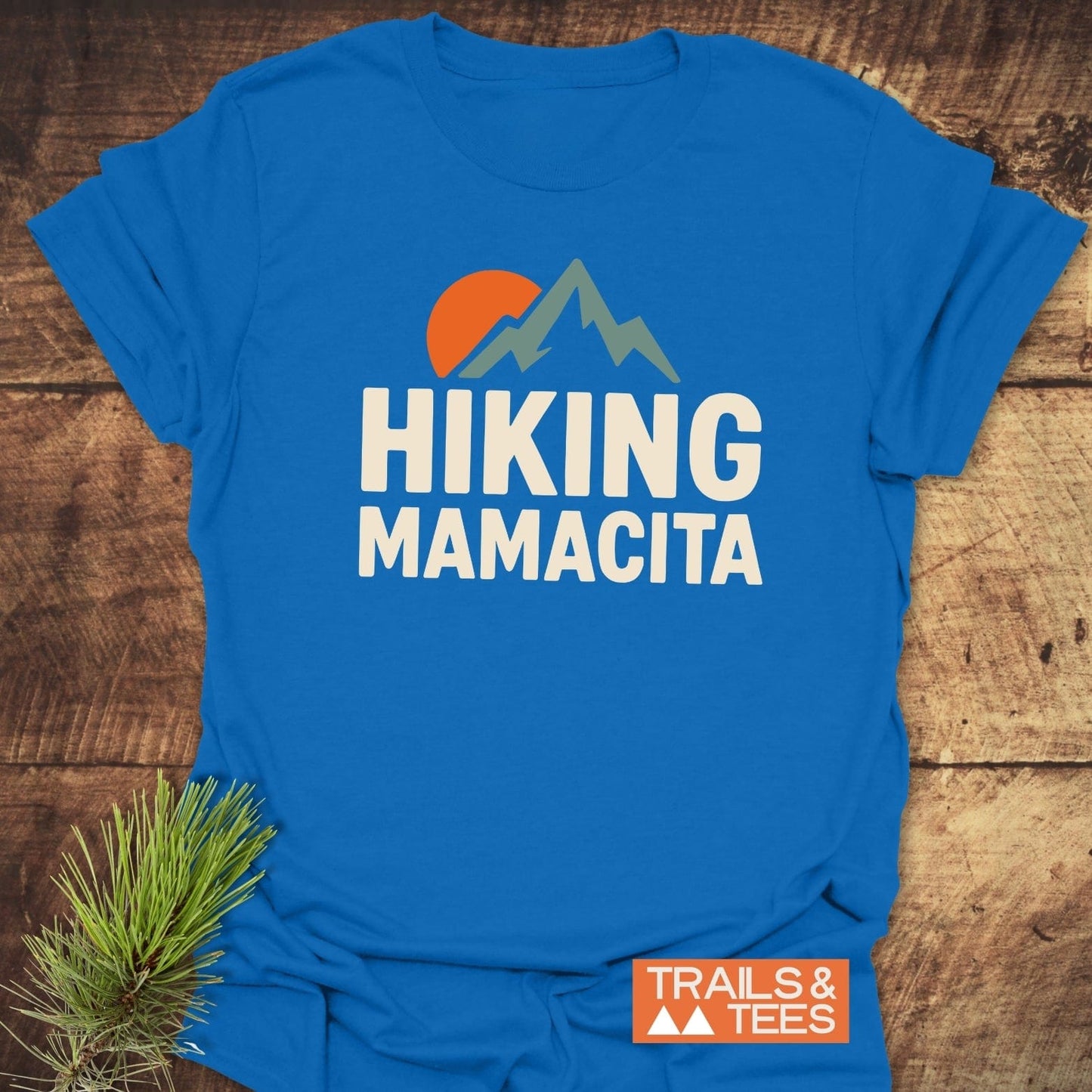 Hiking Mamacita T-Shirt with sunset and mountains graphic, cream text. Soft, lightweight cotton, durable prints. Ideal for outdoor enthusiasts.