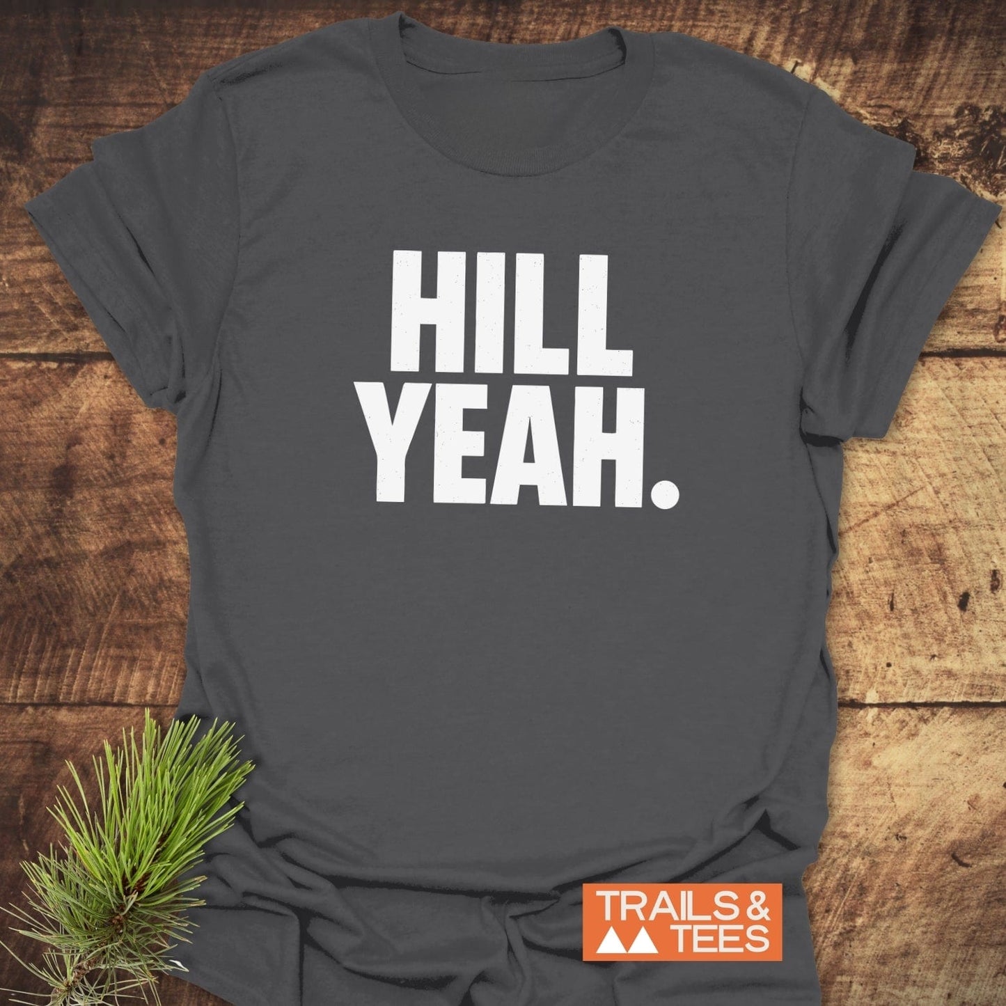 Hill Yeah T-Shirt displayed on wood, featuring white block lettering. Includes Trails & Tees logo. Crafted for comfort with durable prints, ideal for outdoor enthusiasts.