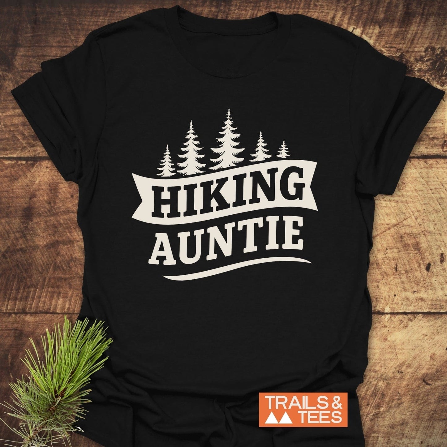 Hiking Auntie T-Shirt featuring evergreen tree graphic and “HIKING AUNTIE” text. Made from soft ring-spun cotton, perfect for outdoor enthusiasts.