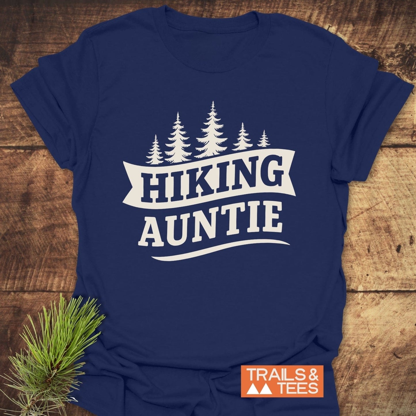 Navy-blue Hiking Auntie T-shirt with pine tree graphic, laid on wood surface, featuring soft cotton and durable print.