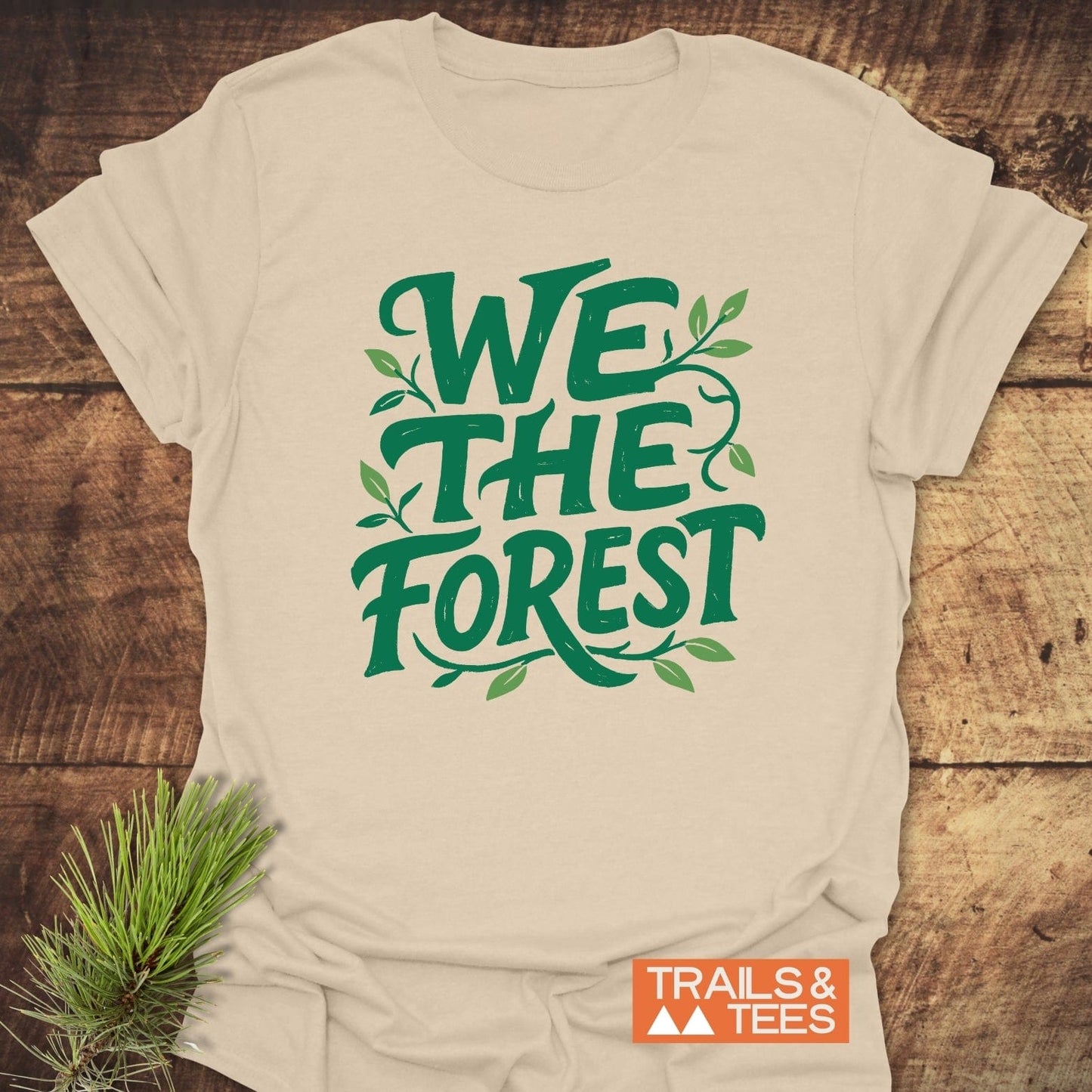We The Forest T-Shirt with green vine print, laid on wood, features 'TRAILS & TEES' logo, crafted from soft ring-spun cotton, designed for outdoor enthusiasts.