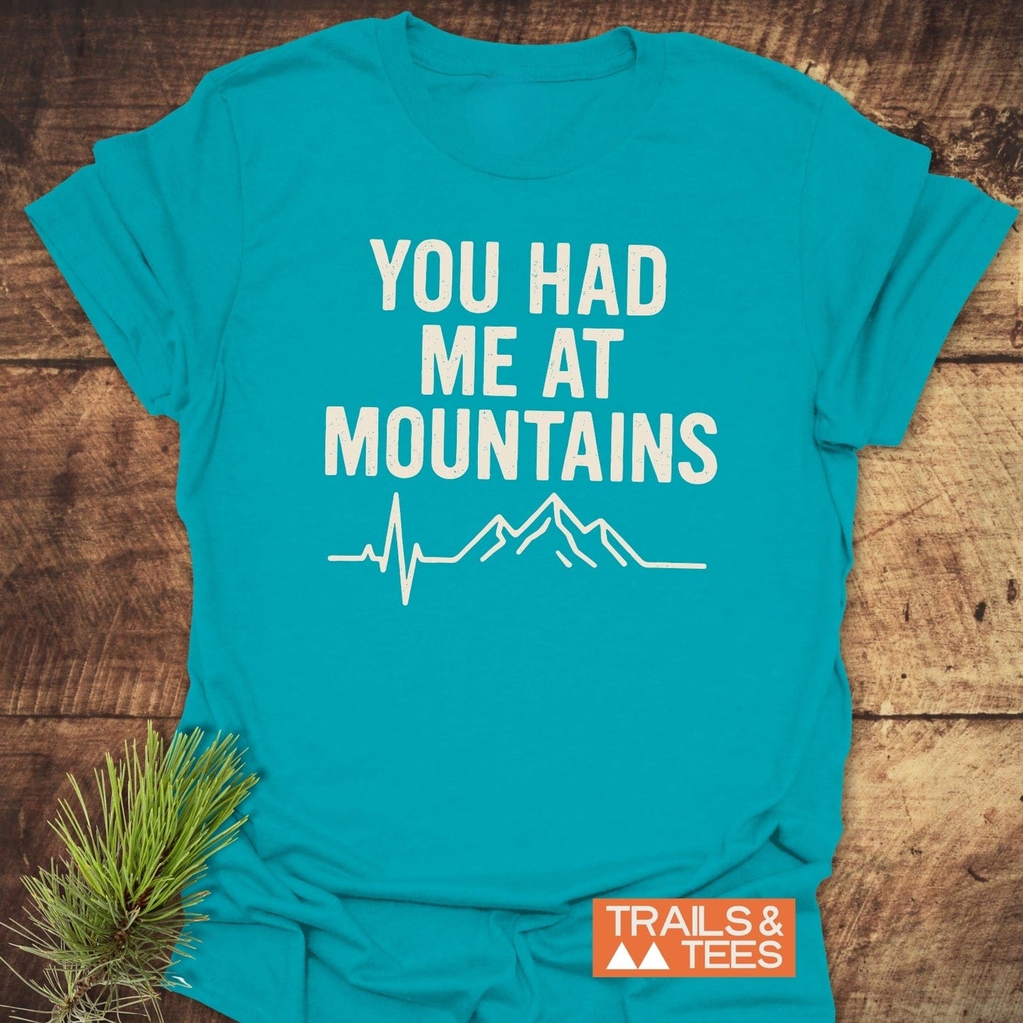 You Had Me At Mountains T-Shirt featuring a mountain silhouette and heartbeat design, crafted from soft cotton for outdoor enthusiasts. Includes Trails & Tees logo.