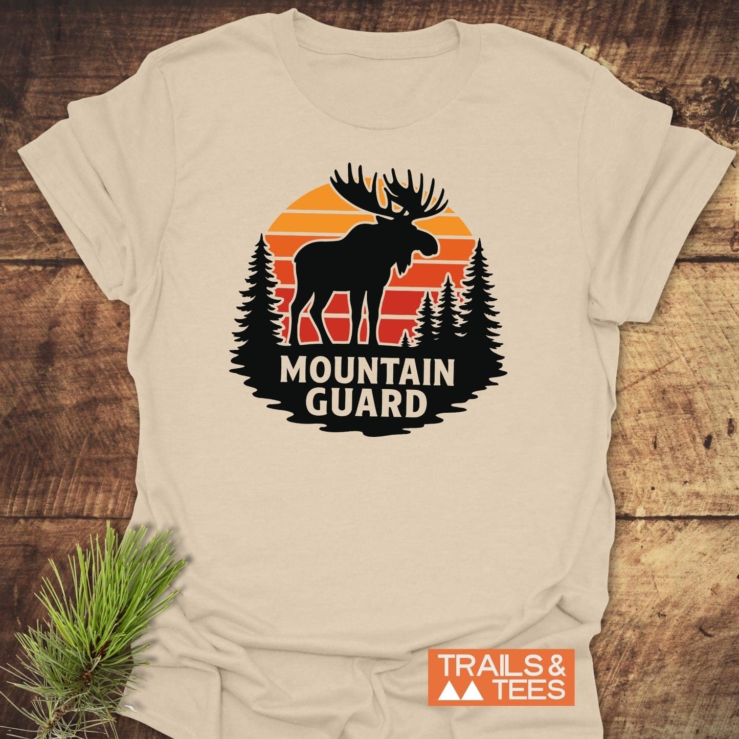 Mountain Guard Moose T-Shirt featuring a moose and pine trees graphic with TRAILS & TEES logo, showcasing outdoor-inspired design on soft, durable cotton.